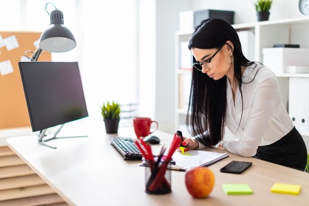 A young girl with glasses, wearing a white blouse and black trousers, works in the office. The girl has long straight black hair. photo with depth of fieldの写真素材