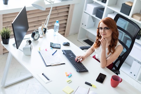 A red-haired young girl with glasses, a white blouse and a red skirt is working in the office. photo with depth of fieldの写真素材