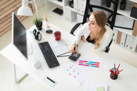 Beautiful young girl with blond hair in a white jacket and black blouse is working in the office. photo with depth of fieldの写真素材