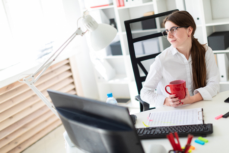 Charming red-haired young girl in glasses and a white blouse is working in a bright office. photo with depth of field.の写真素材