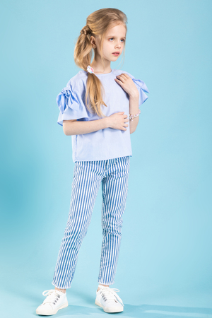 A teenage girl in a blue T-shirt, striped trousers and white sneakers is having fun on a light blue background.の写真素材