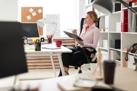 Beautiful young girl with blond hair in a pink blouse is working in the office. photo with depth of fieldの写真素材