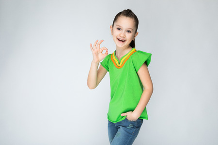 Girl in green t-shirt and blue jeans on grey background.の写真素材
