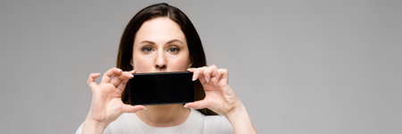 Half-length portrait of attractive plus-size woman in white T-shirt covering her mouth with mobile...