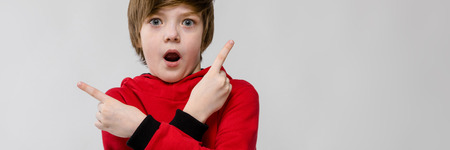 Portrait of small adorable thinking stylish confident caucasian guy in red sweater standing in studio looking in camera holding hands cross to cross showing on blank area astonished.の写真素材