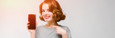 Beautiful young girl posing on gray background. The girl is holding a black phone in her handの写真素材