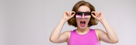 Beautiful young girl posing on gray background. Beautiful girl in square glasses dancesの写真素材