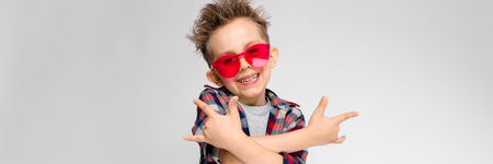 Charming happy child on gray background. The boys hair is up. The boy has a hairstyle. The boy shows the goatの写真素材