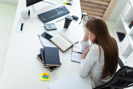 Cute young girl working in a bright office. Young girl in white blouse and black trousers. She has long brown hair. Girl with glasses and beautiful makeup. photo with depth of fieldの写真素材