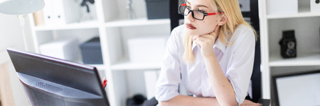 Beautiful young girl working in a bright office at a computer Desk. The girl has white hair and wearing glasses. Shes wearing a white shirt and black pants. photo with depth of fieldの写真素材