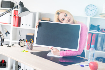 Cute young girl standing at a table in a bright office. She hugs the monitor. She has white hair. Shes wearing a pink jacket and black pants. photo with depth of fieldの写真素材