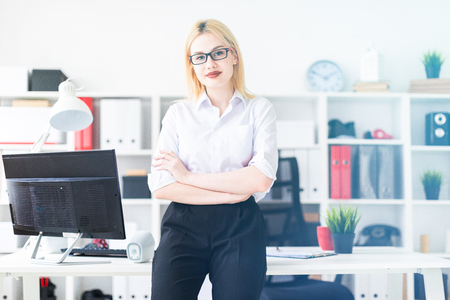 Beautiful young girl working in a bright office at a computer Desk. The girl has white hair and wearing glasses. Shes wearing a white shirt and black pants. photo with depth of fieldの写真素材