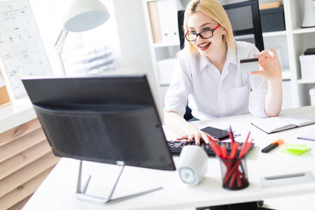 Beautiful young girl working in a bright office at a computer Desk. The girl has white hair and wearing glasses. Shes wearing a white shirt and black pants. photo with depth of fieldの写真素材