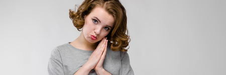 Beautiful young girl posing on gray background. Sad girl folded her hands togetherの写真素材