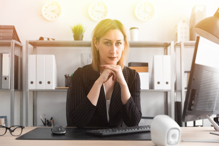Beautiful young girl working in a bright office. The girl has blond hair. She is wearing a light blouse and a striped jacket. photo with depth of fieldの写真素材