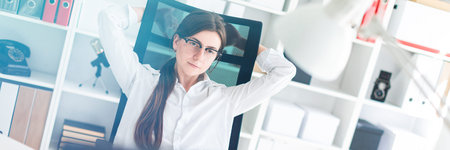 Charming red-haired young girl in glasses and a white blouse is working in a bright office. photo...