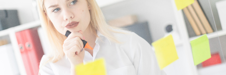 Cute young girl working in a bright office. shes behind the glass with the stickers. Girl drinking coffee and taking notes with a marker. The girl has white hair and wearing glasses. Shes wearing a white shirt and black pants. photo with depth of fieldの写真素材