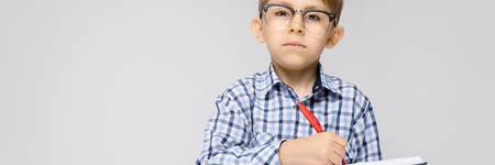 Portrait of a boy on a gray background. A boy with glasses. The boy holds a notebook and a red pen in his hands. A boy makes notes in a notebookの写真素材