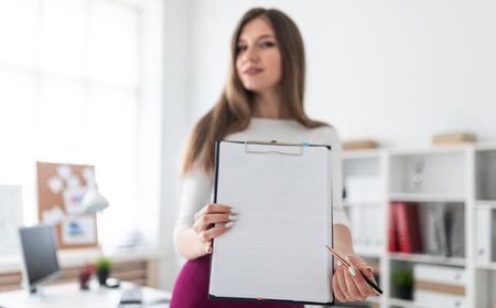 A nice girl works in a bright office. The girl is dressed in a light blouse and a Burgundy skirt. She has long dark hair and beautiful makeup. photo with depth of field. Photo with depth of field, highlighted focus on white sheet.の写真素材