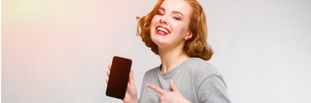 Beautiful young girl posing on gray background. The girl is holding a black phone in her hand
