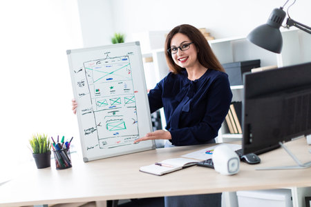 Beautiful girl working in a bright office. The girl is dressed in a light blouse and dark trousers....