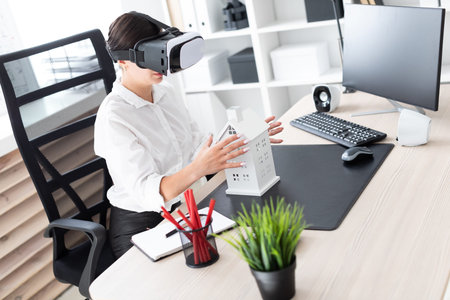 A beautiful young girl looks through virtual reality glasses at the layout of the house. She has...