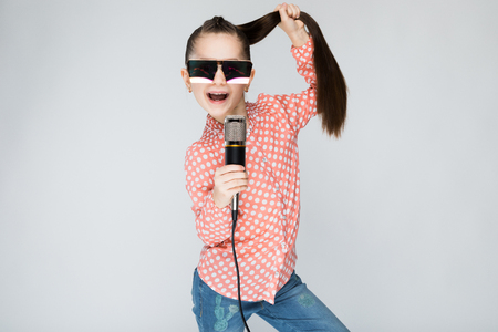 Girl in orange shirt, glasses and blue jeans on grey background.の写真素材