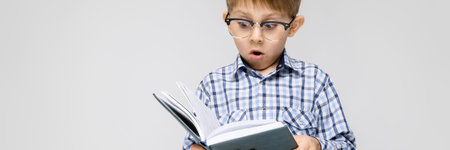 Portrait of a boy on a gray background. A boy with glasses. The boy is reading a book