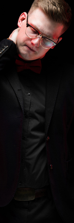 Young caucasian elegant serious smart successful business man in black suit with bow-tie standing in office looking away sad disappointed tired holding hand on his neck.の写真素材