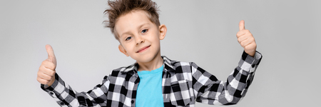 Charming happy child on gray background. The boys hair is up. The boy has a hairstyle. Boy shows thumb with classの写真素材