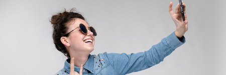 Young girl in round glasses on a gray background. Portrait of a young beautiful girl. Charming girl in a blue denim shirt.の写真素材