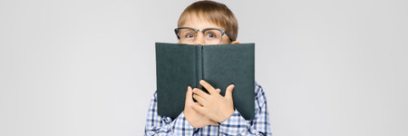 Portrait of a boy on a gray background. A boy with glasses. The boy closed the face book
