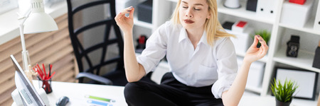 Cute young girl working in a bright office. She sits on the table in the Lotus position and relaxes. The girl has white hair and wearing glasses. Shes wearing a white shirt and black pants. photo with depth of fieldの写真素材