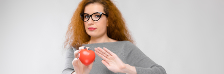 Portrait of attractive smiling woman in dress on grey background with copyspace rejecting plastic heart with her palm gesture.の写真素材