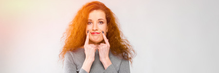 Pretty caucasian young girl with red lips and curly hair looking in camera standing in office showing sad signの写真素材
