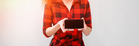 Portrait of attractive woman in checkered dress holding mobile phone presenting it isolated on grey background with copyspace digital advertising concept.の写真素材