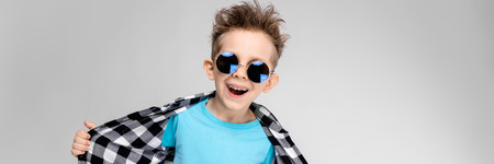 Charming happy child on gray background. The boys hair is up. The boy has a hairstyle. The boy in round sunglassesの写真素材
