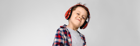 Charming happy child on gray background. The boys hair is up. The boy has a hairstyle. the boy has red hair. A boy in red headphones.の写真素材