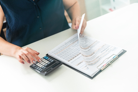 Graceful womens hands leaf through the form and click on the calculator. Charming young girl working in a bright office. photo with depth of fieldの写真素材