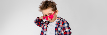 Charming happy child on gray background. The boys hair is up. The boy has a hairstyle. The boy laid his hand on his headの写真素材