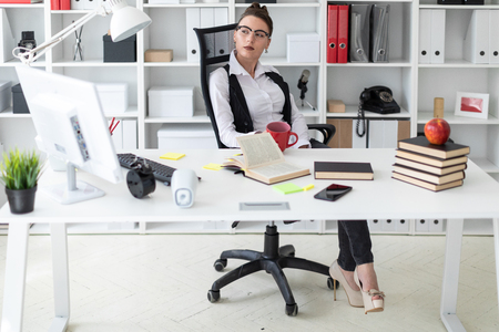 A beautiful young girl with a bunch on her head in a white shirt and a black waistcoat works in a bright office. photo with depth of fieldの写真素材