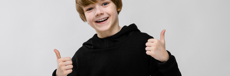 Portrait of cute little boy wearing black hoody and holding thumbs up in approval sign gesture isolated on grey background with copyspace childrens fashion concept.の写真素材