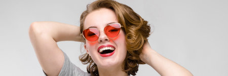 Beautiful young girl posing on gray background. Girl in red glasses