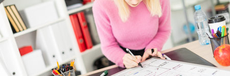 Cute young girl standing at a table in a bright office. Shes holding a marker. Before the girl on...