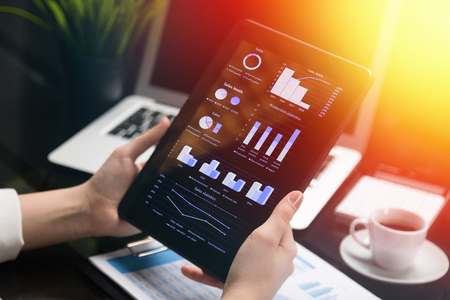 Womens Hands hold black tablet with blank screen on background of sheets with diagrams. Businesswoman analyzes market information on modern digital tablet computer. insurance agent gets acquainted with statisticsの写真素材