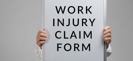 hands in a shirt with a poster work injury claim form isolated in a light Studio. Businessman holds...