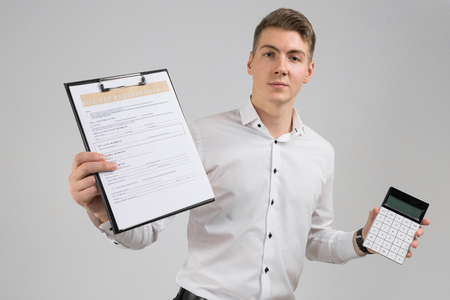 Young businessman with questionnaire and modern calculator in his hands. Business young man in white shirt in bright Studio alone. place for labelの写真素材