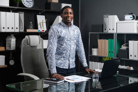 successful African businessman in an official shirt works in bright office. African-American man is...