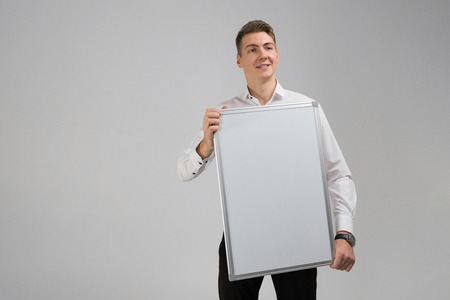 young businessman closed part of himself with white poster in his hands. Business young man in white shirt in bright Studio alone. place for labelの写真素材