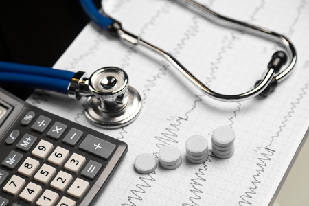 Steps of tablets next to calculator and a stethoscope on background of an electrocardiogram. Cardio therapist assistance, physical make cardiac physical. concept of medicine and health care. empty doctor workplace with a stethoscope and pillsの写真素材